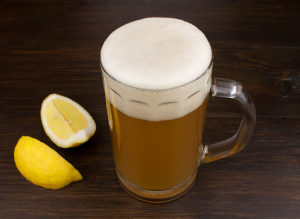 Glass of wheat beer and lemon on wooden background